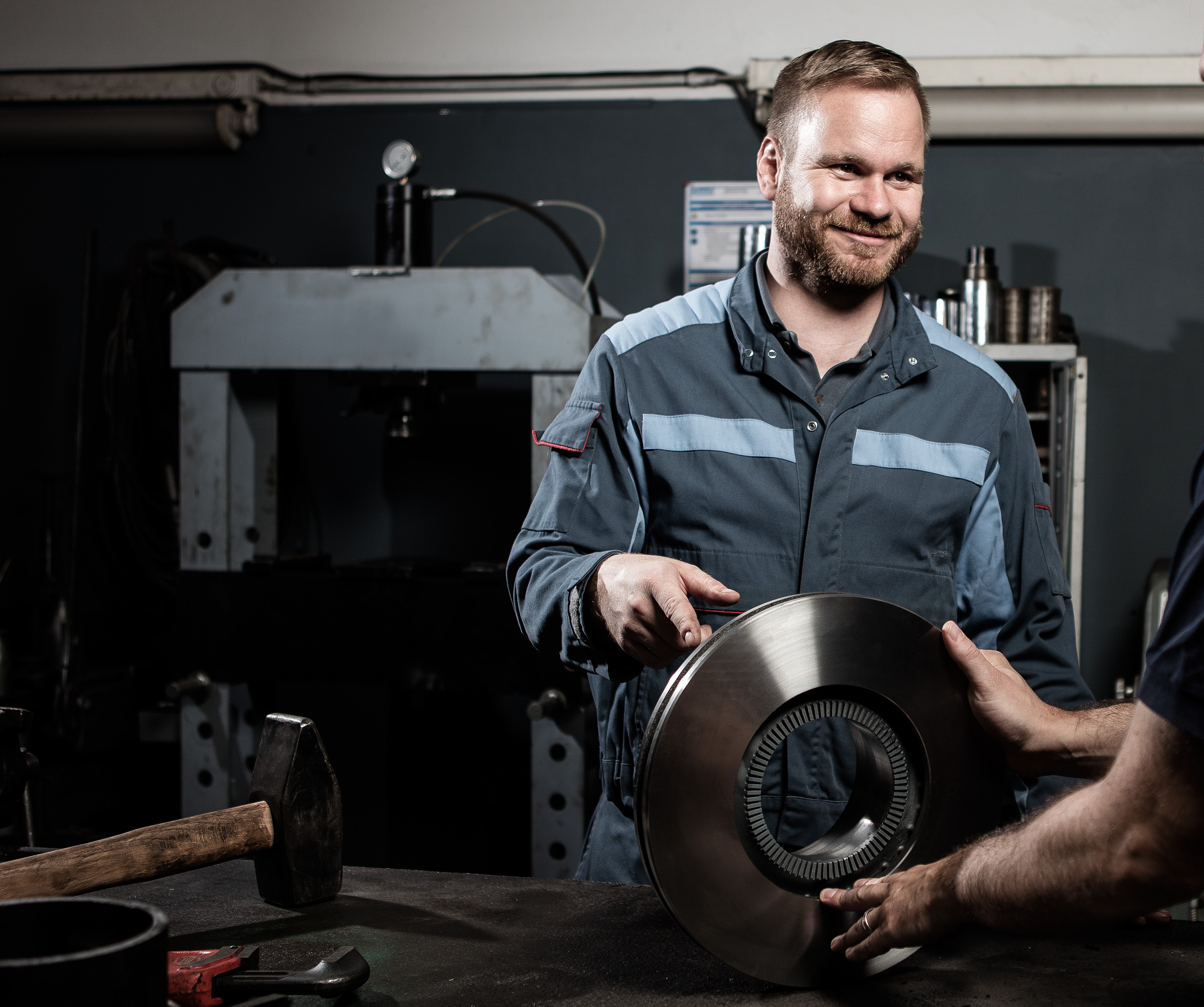 Mitarbeiter in Werkstatt übergibt Metallbauteil an Kollegen in industrieller Umgebung